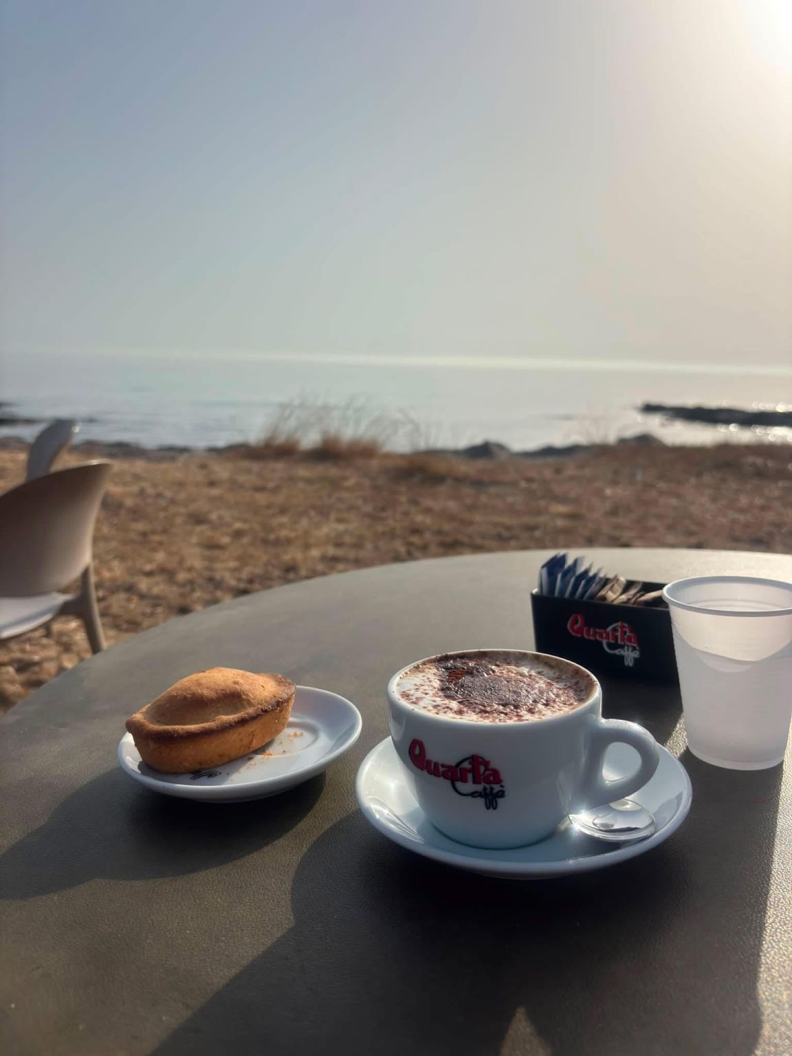 Cappuccino i włoskie ciastko na stoliku nad morzem